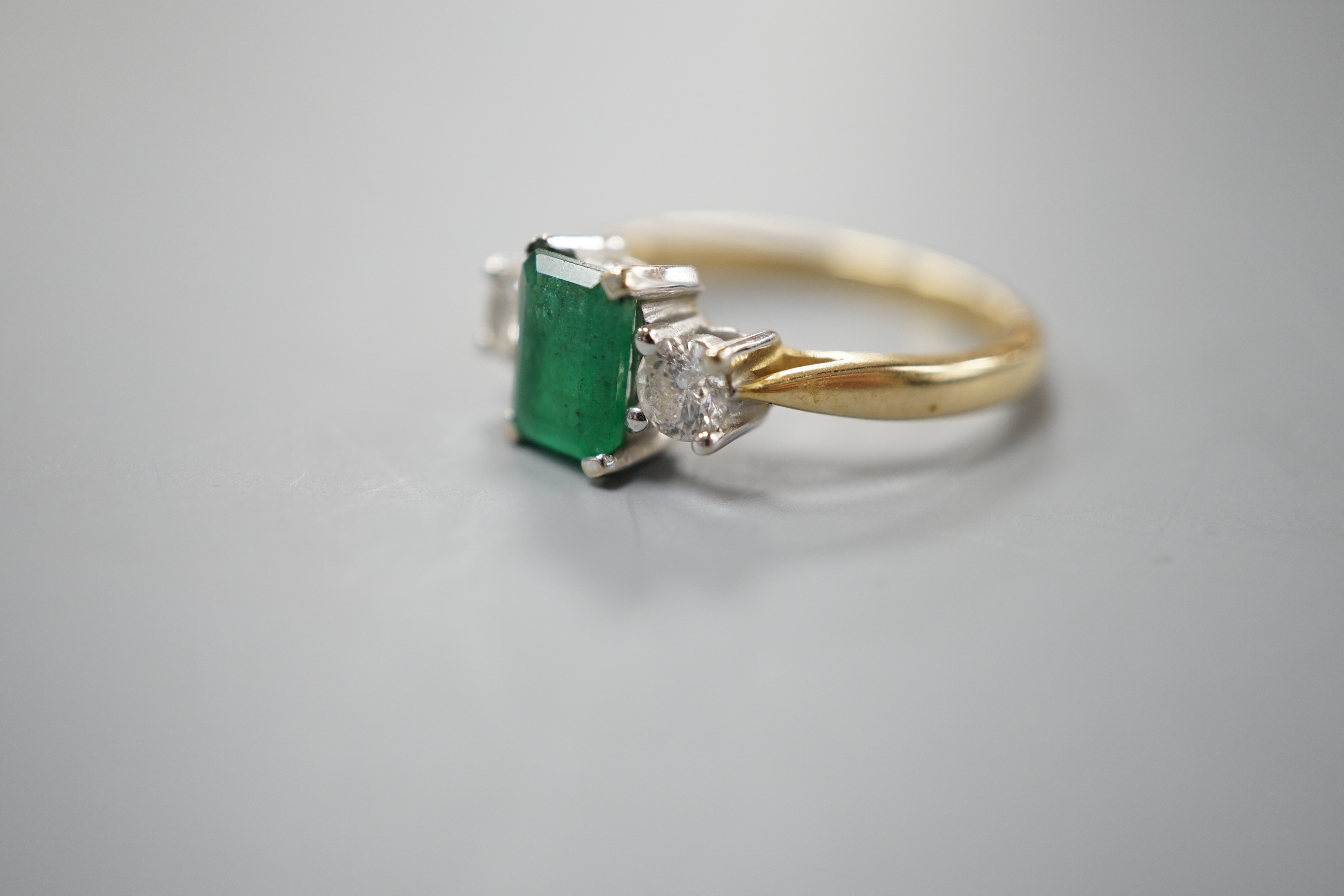 A modern 18ct gold, emerald and diamond set three stone ring, size N, gross weight 3.5 grams.